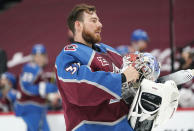 Colorado Avalanche goaltender Philipp Grubauer adjusts the straps on his mask as he heads back to the net during a timeout in the first period of an NHL hockey game against the Arizona Coyotes, Monday, April 12, 2021, in Denver. (AP Photo/David Zalubowski)