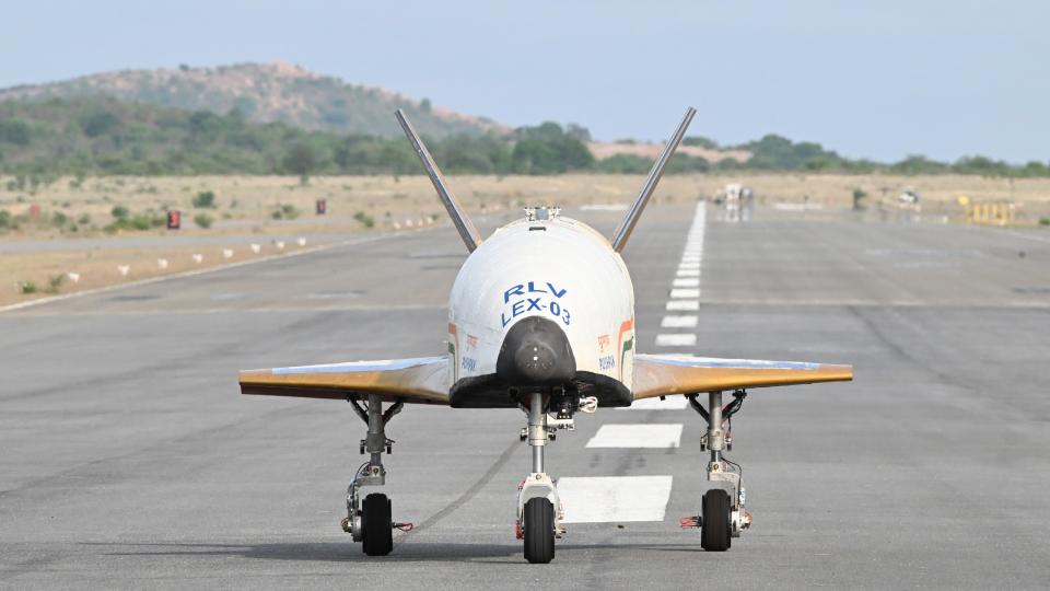 a white airplane with no windows or cockpit canopy lands on a runway surrounded by tropical vegetation