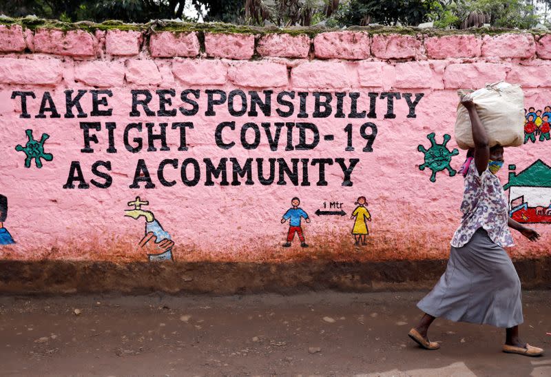 FILE PHOTO: A woman walks past a wall painted with a slogan calling for action against the coronavirus disease (COVID-19) in the Kibera slum of Nairobi