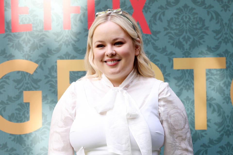 Nicola Coughlan smiles at a Netflix event, wearing a white blouse with a bow