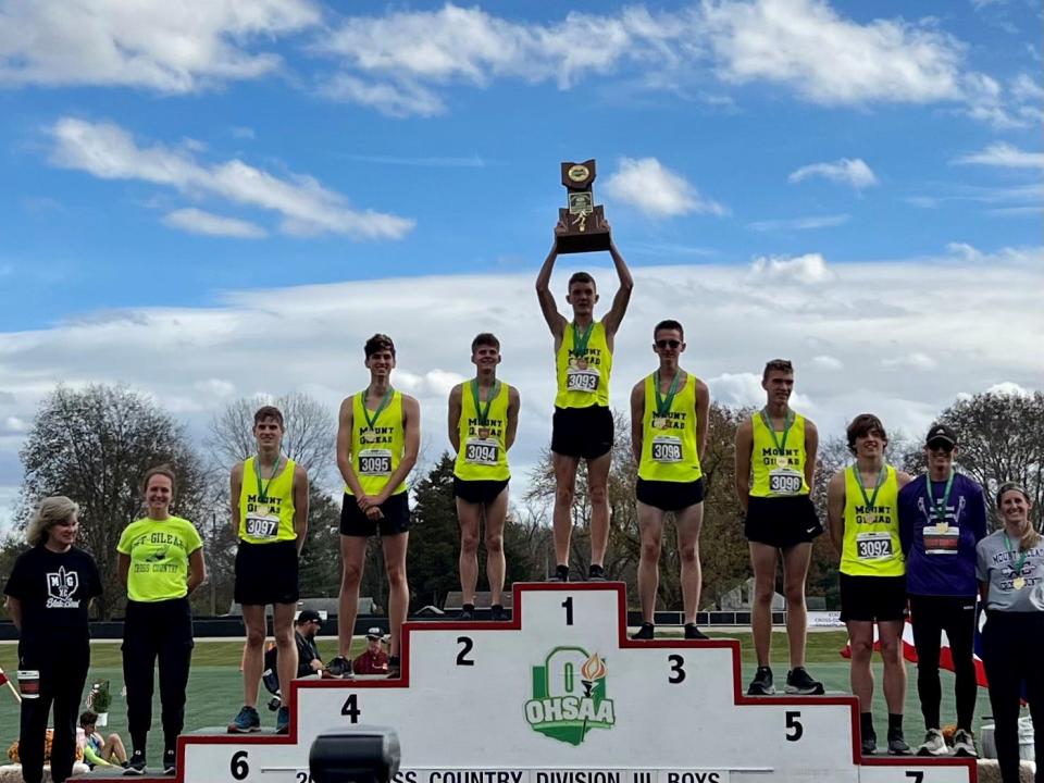 Mount Gilead's Will Baker holds the Division III boys cross country state championship trophy above his head as the team poses for pictures on the podium Saturday at Fortress Obetz.