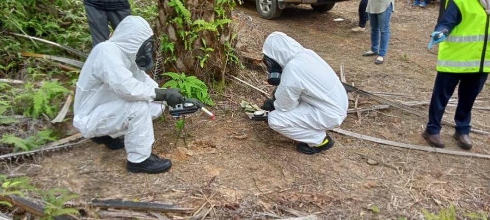 two people in white hazmat suits holding sensors crouch in a forest