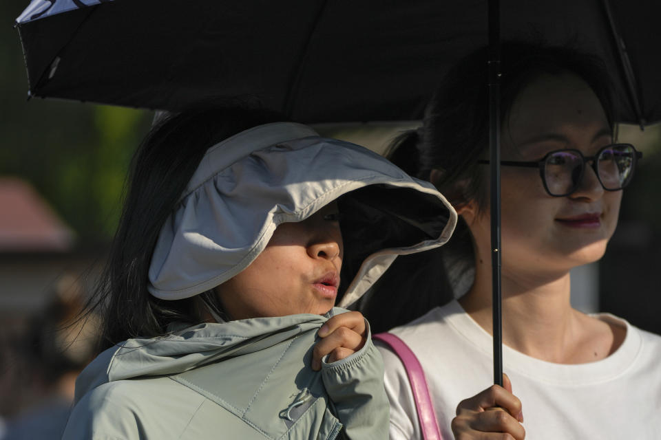 A woman wearing a hat and sun protective clothing reacts from an unseasonably hot day in Beijing, Sunday, June 16, 2024. China is being buffeted by two weather extremes, with heavy rain and flooding in parts of the south and a heat wave and potential drought in the north. (AP Photo/Andy Wong)