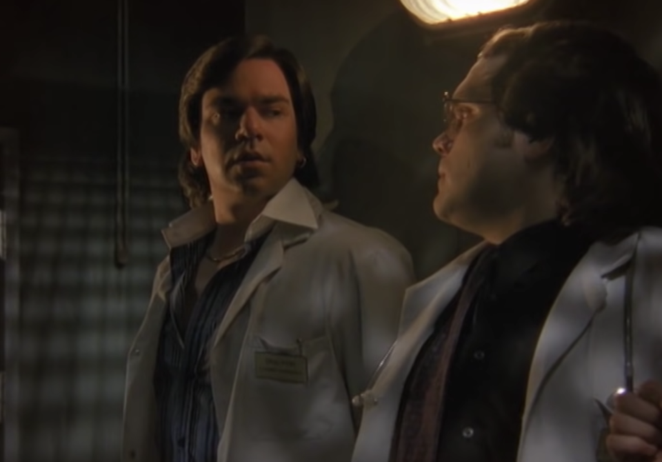 Two men look at each other while wearing white lab coats