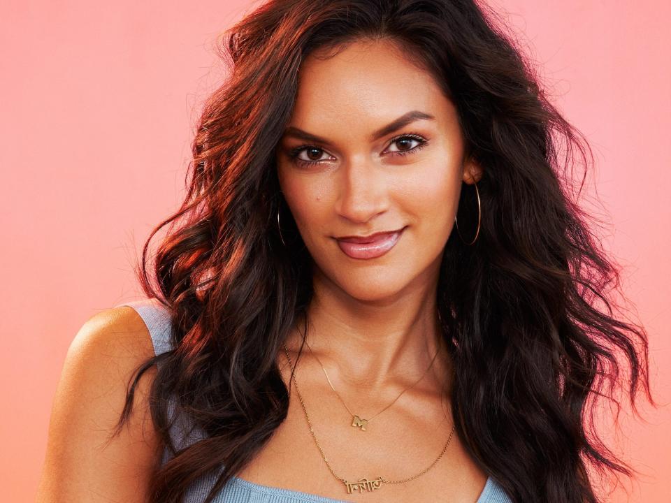 Malina poses for photos in a blue tank top and gold jewelry.