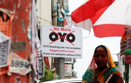 A woman walks pasts a sign against Oy, placed outside a hotel in New Delhi