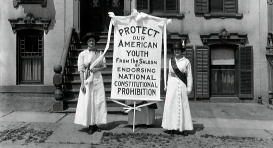 Two women standing in a street with a sign "Protect our American youth from the saloon"