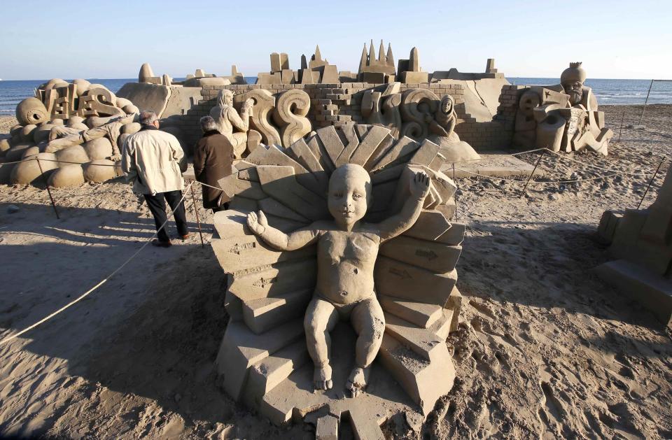 People walk in a nativity scene made of sand on a beach in Salou