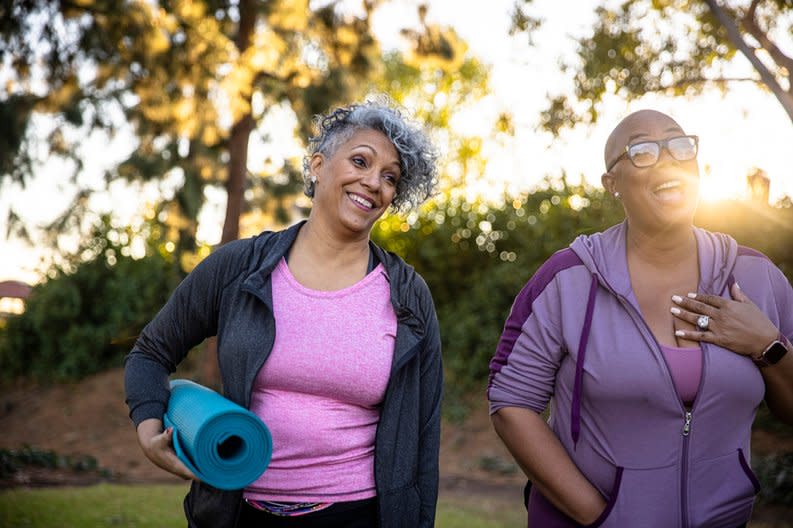 Two smiling middle age adults outdoors with yoga mats.