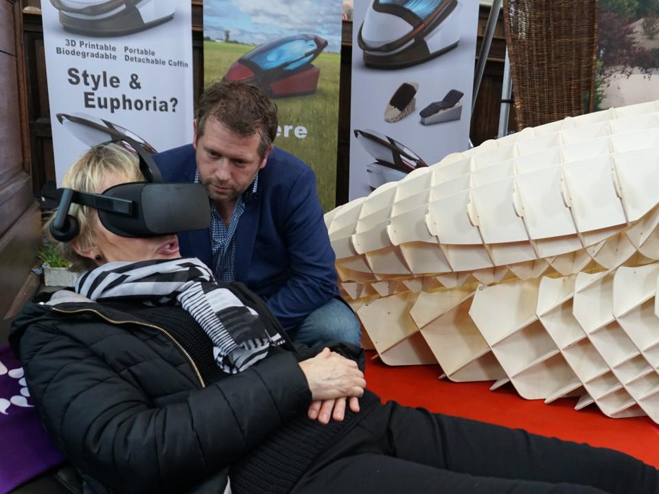 Dutch designer Alexander Bannink explains how the "Sarco" euthanasia pod works as a woman experiences sitting in the device by wearing virtual reality glasses, on April 14, 2018 at the Amsterdam Funeral Expo.