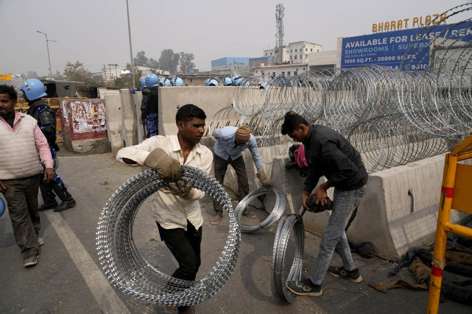 Workers put up barbed wire on top of barricades on a major highway at Singhu near New Delhi to stop thousands of protesting farmers from entering the capital, India, Tuesday, Feb.13, 2024. Farmers, who began their march from northern Haryana and Punjab states, are asking for a guaranteed minimum support price for all farm produce. (AP Photo/Manish Swarup)