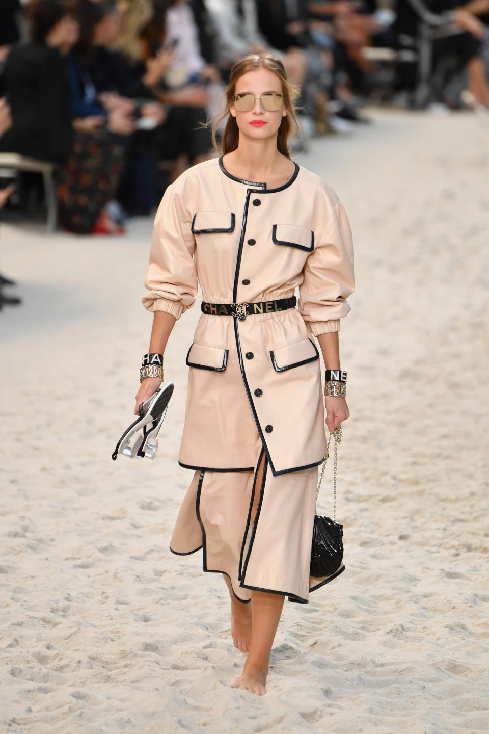 <p>An stürmischeren Tagen am Meer eignet sich dieses Chanel-Ensemble im 80er Jahre Vintage-Look: Ein beigefarbener Coat mit gerafften Ärmeln und Ledersaum, sowie der dazu passende Rock mit Beinschlitz. Highlight: Die schwarze Muscheltasche. (Bild: Getty Images) </p>