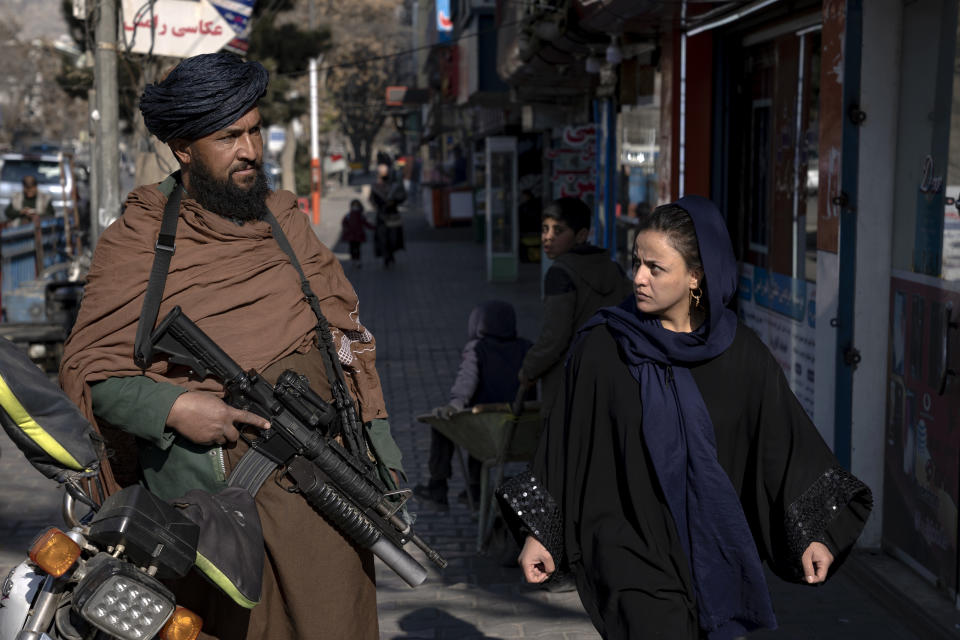 FILE - A Taliban fighter stands guard as a woman walks past in Kabul, Afghanistan, on Dec. 26, 2022. (AP Photo/Ebrahim Noroozi, File)