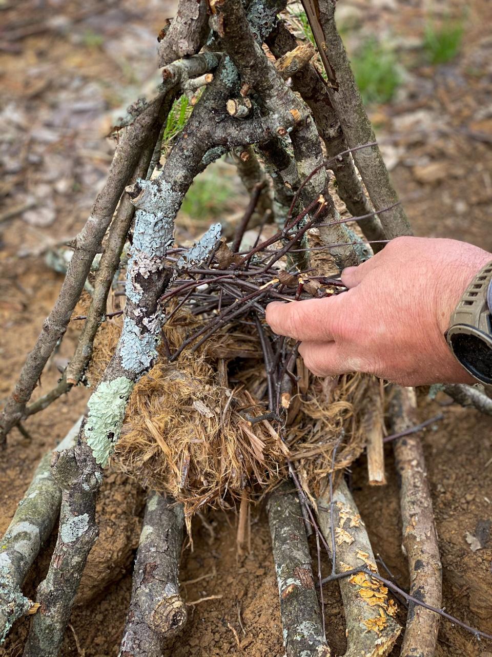 A man places fire tinder into a formation of firewood shaped as a teepee.