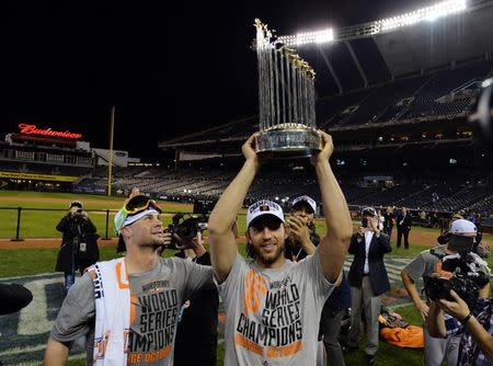Oct 29, 2014; Kansas City, MO, USA; San Francisco Giants starting pitcher Ryan Vogelsong (left) watches as teammate Madison Bumgarner (middle) hoists the Commissioners Trophy after game seven of the 2014 World Series against the Kansas City Royals at Kauffman Stadium. Mandatory Credit: Peter G. Aiken-USA TODAY Sports