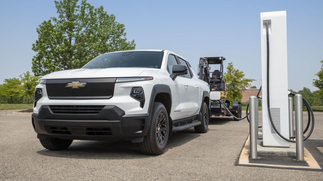 front shot of the silverado ev wt plugged in at a charging station, towing a trailer behind