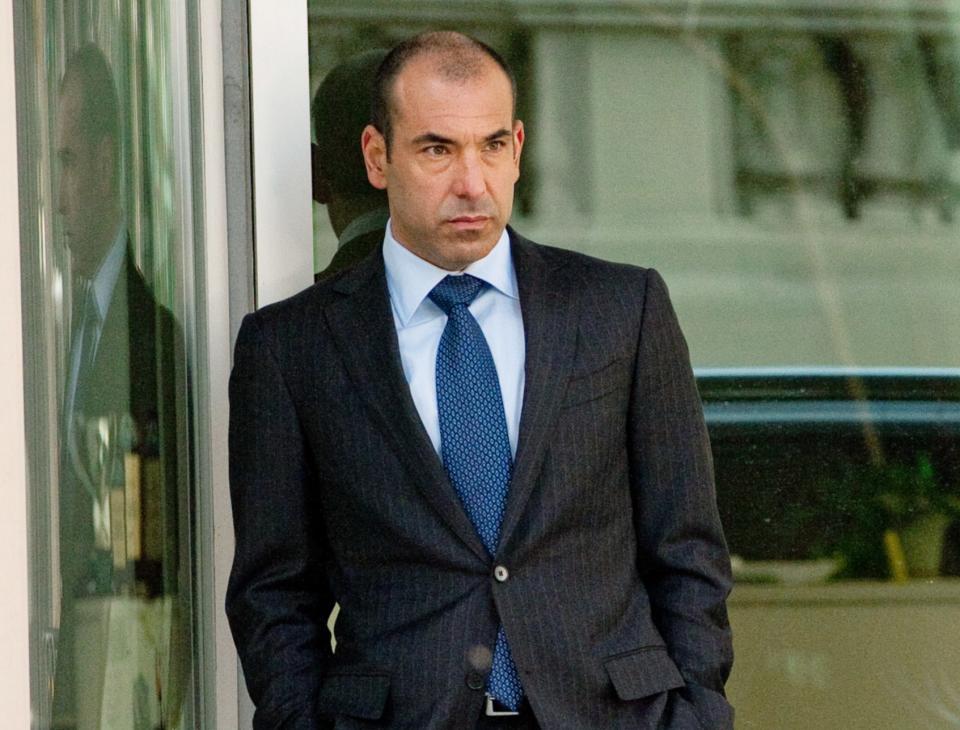 Man in a suit standing by a building, looking pensive