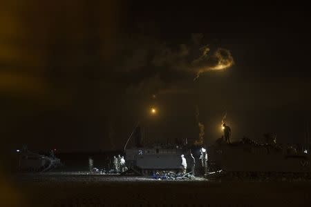 Israeli soldiers stand around their armoured personnel carriers (APCs) across from the northern Gaza Strip, as flares from Israel light the sky, July 18, 2014. REUTERS/ Baz Ratner