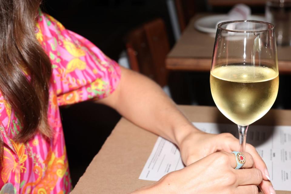 Actress Alison Brie's hands holding the stem of a glass of white wine in a restaurant.