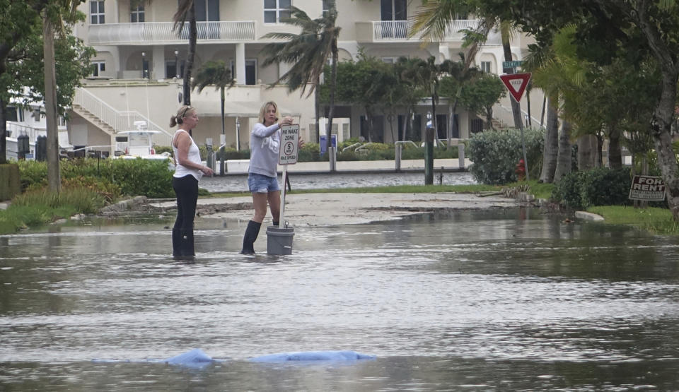 FILE - In this Oct. 5, 2017, file photo, residents move a "no wake," sign through flood waters caused by king tides in Fort Lauderdale, Fla. Federal scientists, according to a report released Wednesday, July 10, 2019, predict 40 places in the U.S. will experience higher than normal rates of so-called sunny day flooding this year due to rising sea levels and an abnormal El Nino weather system. (Joe Cavaretta/South Florida Sun-Sentinel via AP)