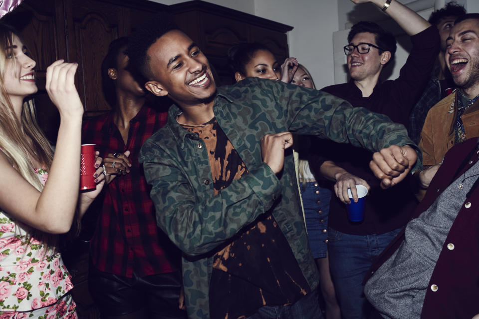 Group of young adults partying, some with drinks in hand, dancing and laughing