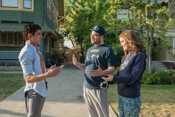 Zac Efron stands and talks to Seth Rogen and Rose Byrne in Neighbors.