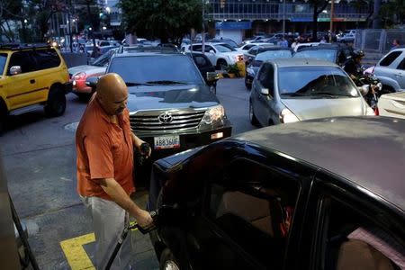 A man pumps gas into a car as people wait in line to fill the tanks of their vehicles at a gas station of the state oil company PDVSA in Caracas, Venezuela March 22, 2017. REUTERS/Carlos Garcia Rawlins