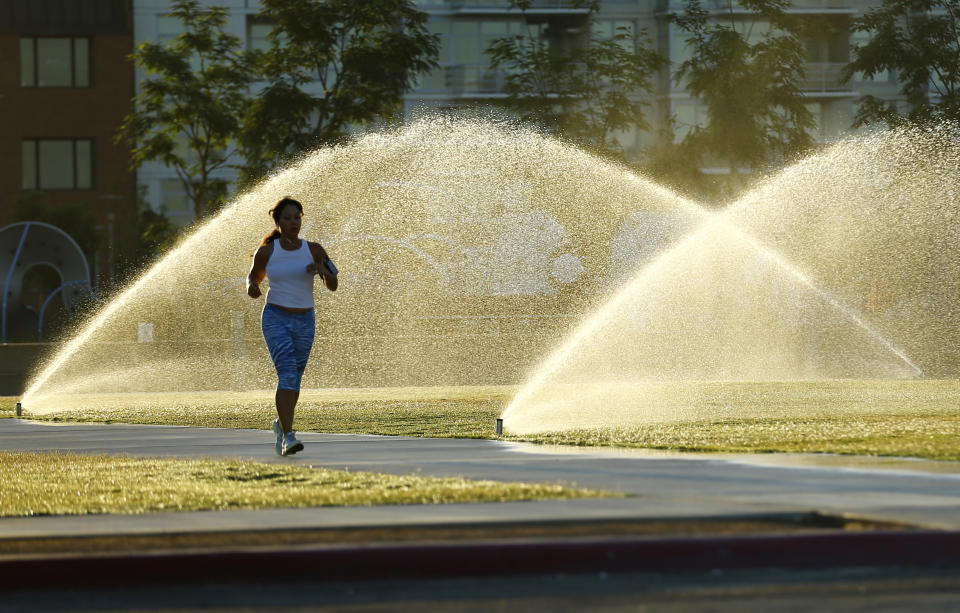 Sprinklers spray water onto grass as a jogger runs through a city park in San Diego.