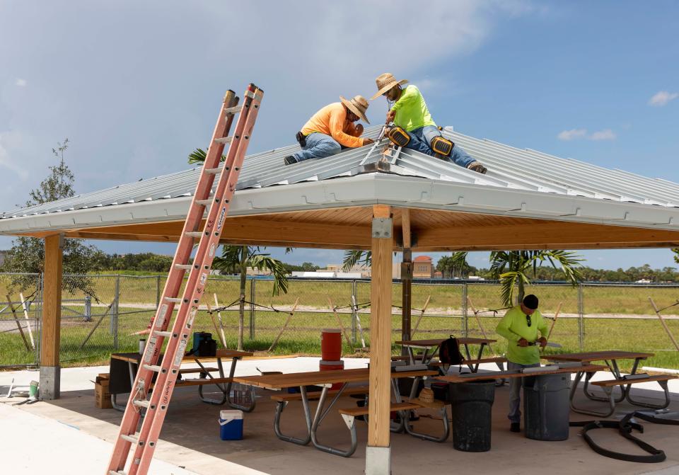 Decktight Roofing Services workers assembly a roof over picnic tables at the Canyon District Park in Boynton Beach on August 2, 2022. 