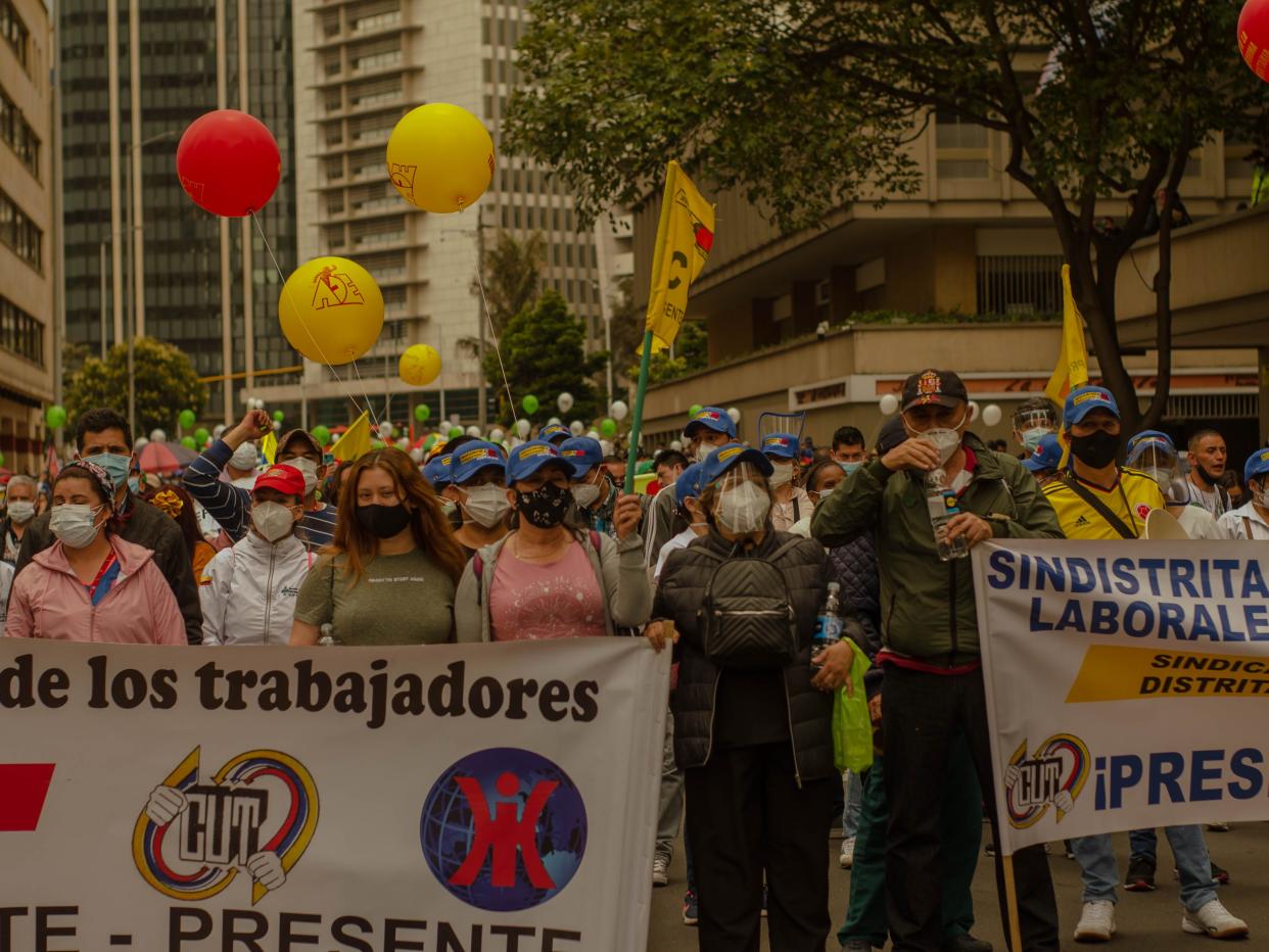 Protesters stand in the street holding signs with balloons behind them.