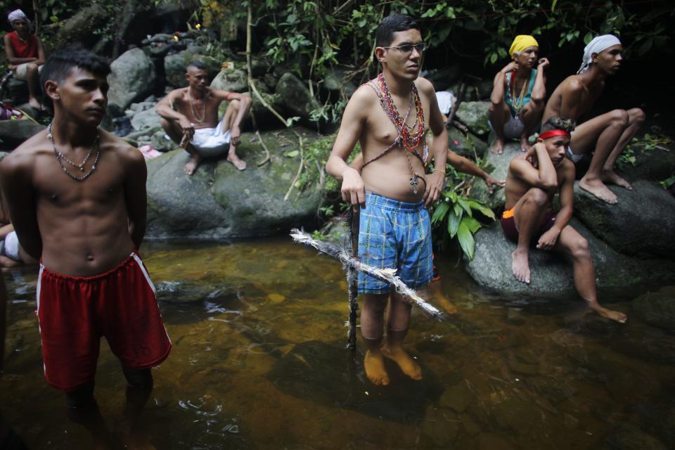 In this photo taken Oct. 12, 2019, men standing in a pool of water watch a spiritual ceremony on Sorte Mountain where followers of indigenous goddess Maria Lionza gather annually in Venezuela's Yaracuy state. Devotees say the number of followers swells as Venezuelans turn for answers to the struggle of daily life outside traditional political system, churches and hospitals. (AP Photo/Ariana Cubillos)