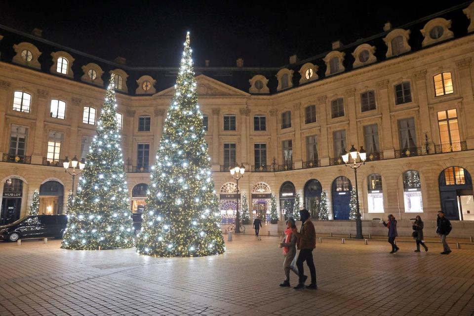 Two people walk by two Christmas trees decorated with lights stand in the Place Vendome in Paris, France, for the holidays.