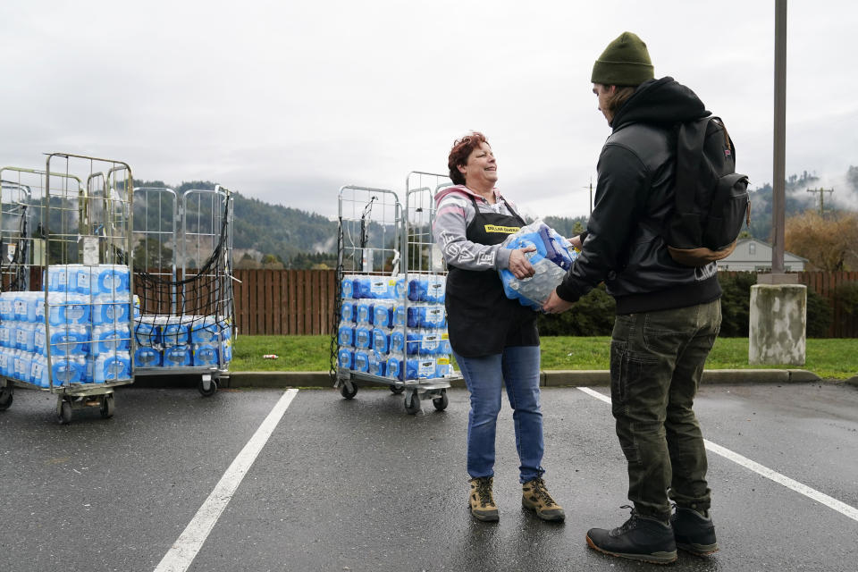 Penny Dunaway, middle, hands out water to a man after an earthquake in Rio Dell, Calif., Tuesday, Dec. 20, 2022. A strong earthquake shook a rural stretch of Northern California early Tuesday, jolting residents awake, cutting off power to 70,000 people, and damaging some buildings and a roadway, officials said. (AP Photo/Godofredo A. Vásquez)