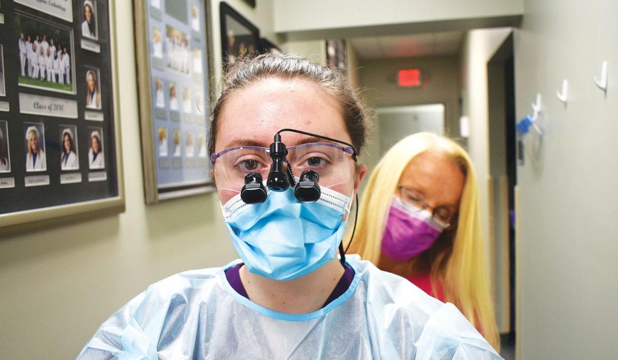 Dental hygiene program director Melinda Gill helps Roane State student Natasha McNeil into the mandatory garb she wears while working with patients. Still to be put on: a hair covering and a face shield.