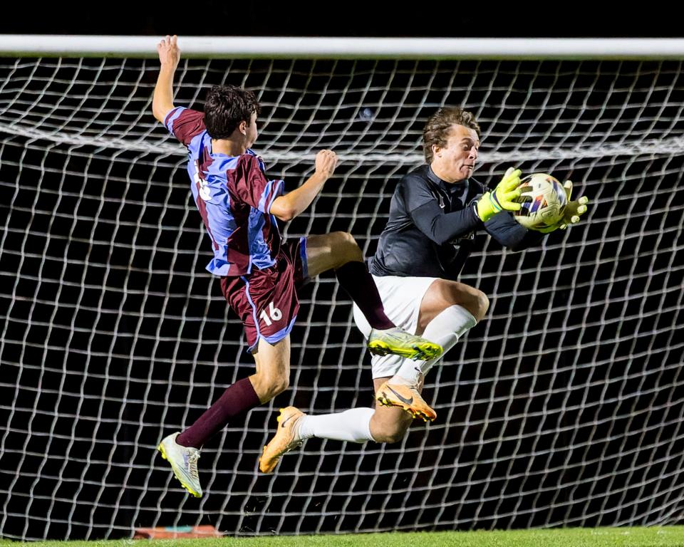 Brighton goalie Charlie Burchfield makes one of his eight saves while Okemos' Logan Herschleib charges the net during a first-round district soccer game Thursday, Oct. 12, 2023.