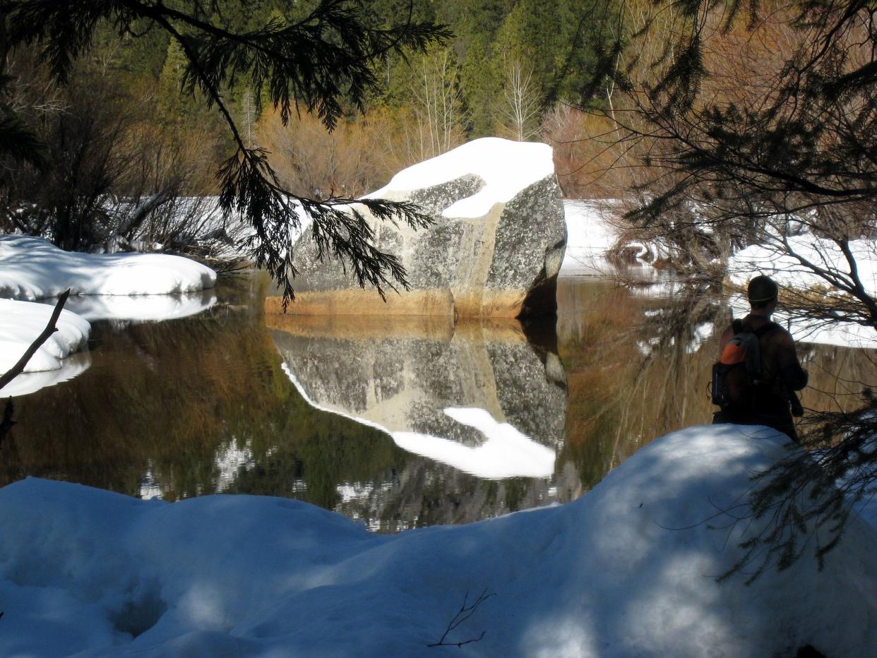 Lake surrounded by snow with a large rock in the middle of the lake being reflected in the water.