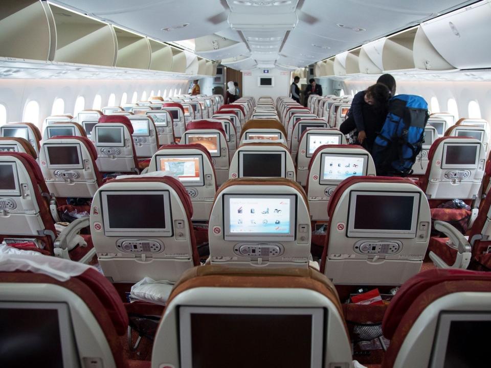 Interior of current 787 with red and yellow seats and dated screens.