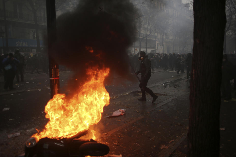 Youths stand behind a burning vehicle during a demonstration in Paris, Thursday, Dec. 5, 2019. Small groups of protesters are smashing store windows, setting fires and hurling flares in eastern Paris amid mass strikes over the government's retirement reform. (AP Photo/Rafael Yaghobzadeh)