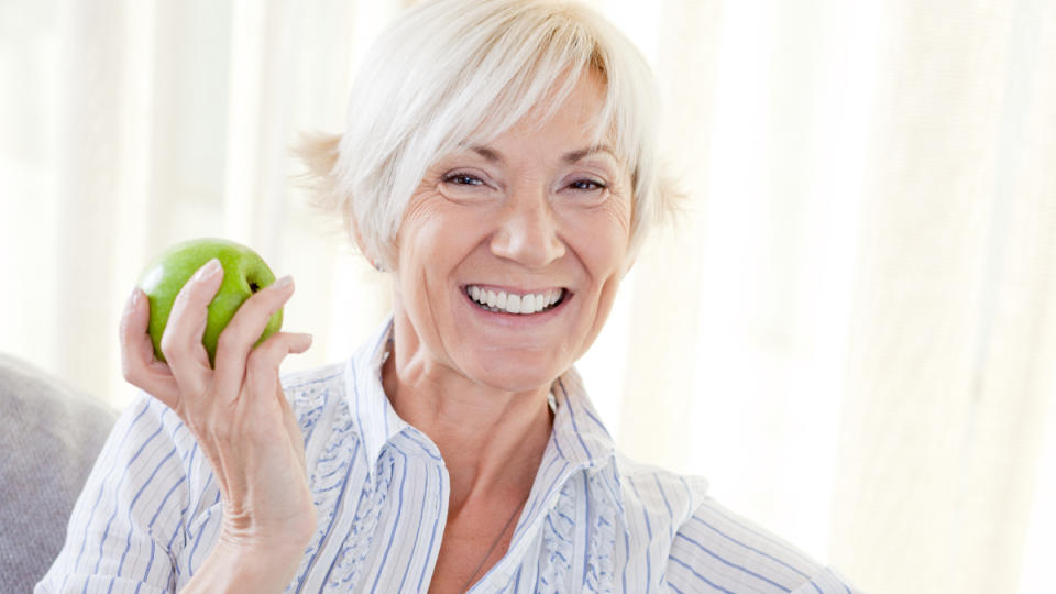 A woman with short grey hair and a striped shirt holding a green apple, which is better than sucralose that may raise your blood sugar