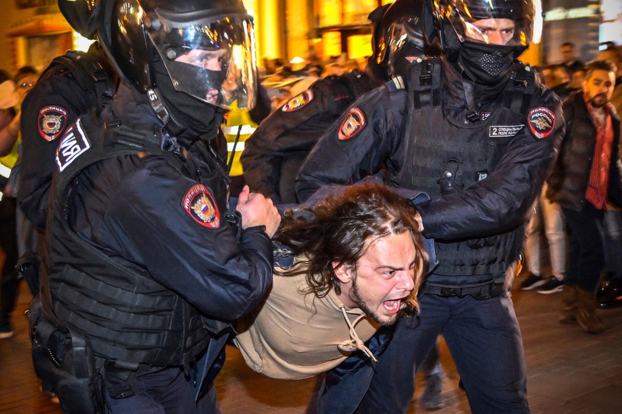Police officers detain a man at a protest as he screams.