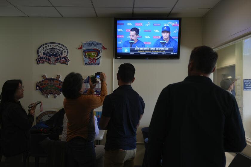 Reporters watch a video screen displaying Los Angeles Dodgers' Shohei Ohtani, right, and interpreter Will Ireton during a news conference at Dodger Stadium in Los Angeles, Monday, March 25, 2024. (AP Photo/Jae C. Hong)