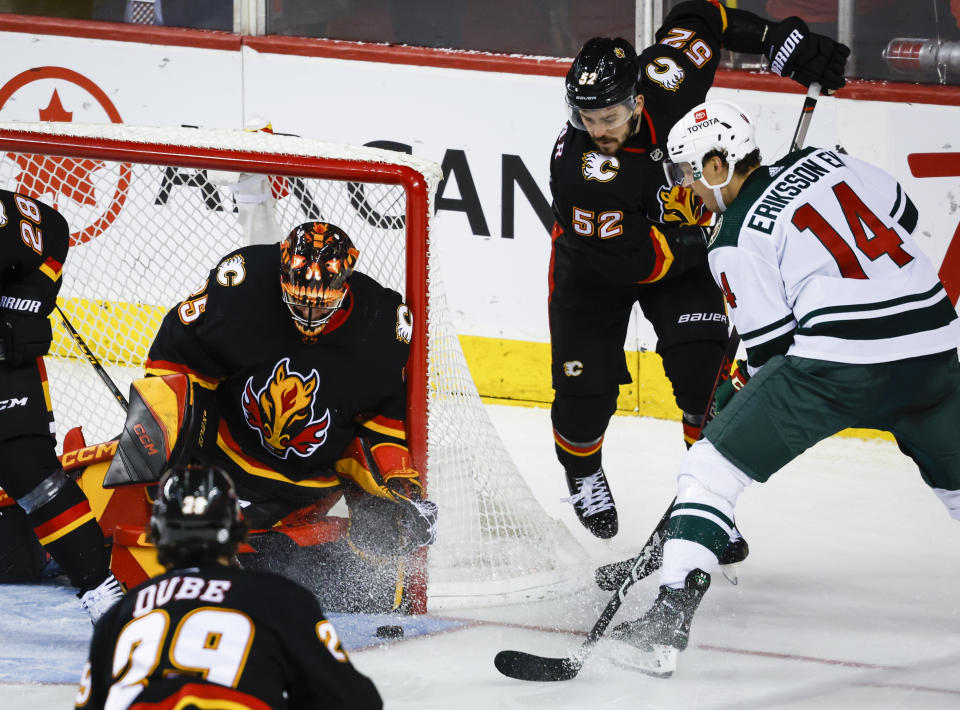 Minnesota Wild forward Joel Eriksson Ek, right, digs for the puck as Calgary Flames goalie Jacob Markstrom, left, and defenseman MacKenzie Weegar watch during the third period of an NHL hockey game Saturday, March 4, 2023, in Calgary, Alberta. (Jeff McIntosh/The Canadian Press via AP)