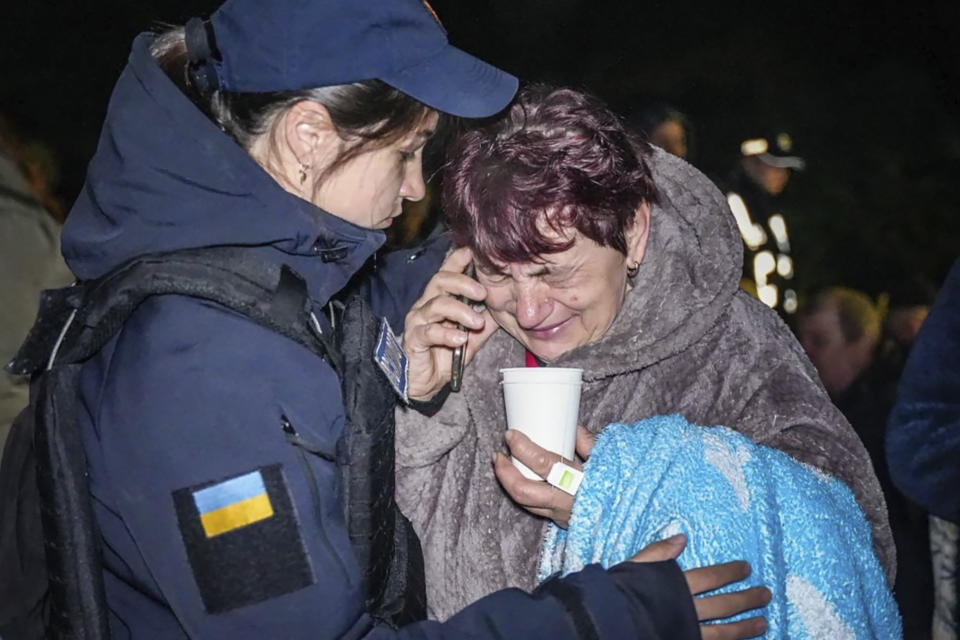 In this photo provided by the Ukrainian Emergency Service, emergency service psychologist, left, comforts a woman at the scene of a building that was damaged by night Russian drone attack in Odesa, Ukraine, Tuesday, April 23, 2024. (Ukrainian Emergency Service via AP)