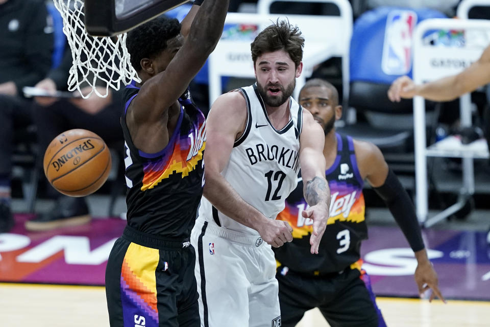 Brooklyn Nets forward Joe Harris (12) passes around Phoenix Suns center Deandre Ayton during the first half of an NBA basketball game, Tuesday, Feb. 16, 2021, in Phoenix.(AP Photo/Matt York)