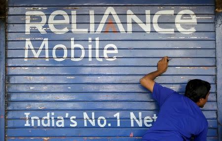 A man opens the shutter of a shop painted with an advertisement of Reliance Communications in Mumbai, November 3, 2015. REUTERS/Shailesh Andrade/Files