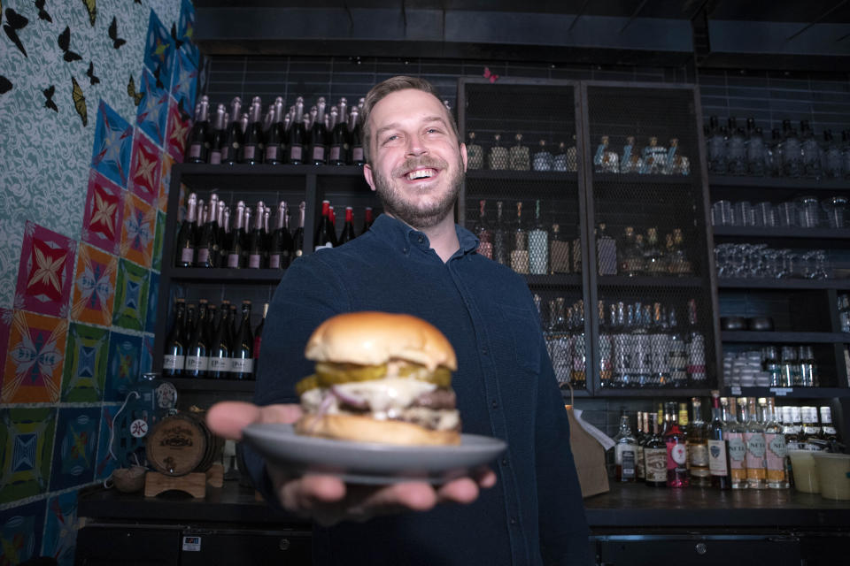 Josh Phillips, the co-owner of Espita, a stylish Mexican restaurant, holds a Ghostburger at his restaurant in downtown Washington, Monday, Feb. 15, 2021. Phillips opened a delivery-only brand called Ghostburger in August to keep Espita’s kitchen running through the winter. He chose burgers because he wanted to reach new customers at a lower price point than Espita. It’s been so successful that Phillips is now scouting for locations for standalone Ghostburger restaurants. (AP Photo/Jose Luis Magana)