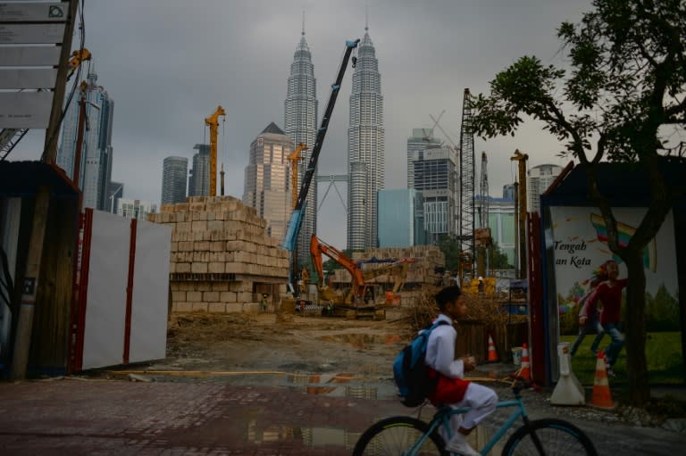 A boy rides a bicycle in front of a construction site as Malaysia's iconic Petronas Twin Towers loom in the background of Kampung Baru enclave in Kuala Lumpur