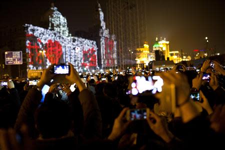 Visitors take pictures and videos during a light show as part of a New Year countdown celebration as part of a New Year countdown celebration on the Bund in Shanghai January 1, 2014. REUTERS/Aly Song