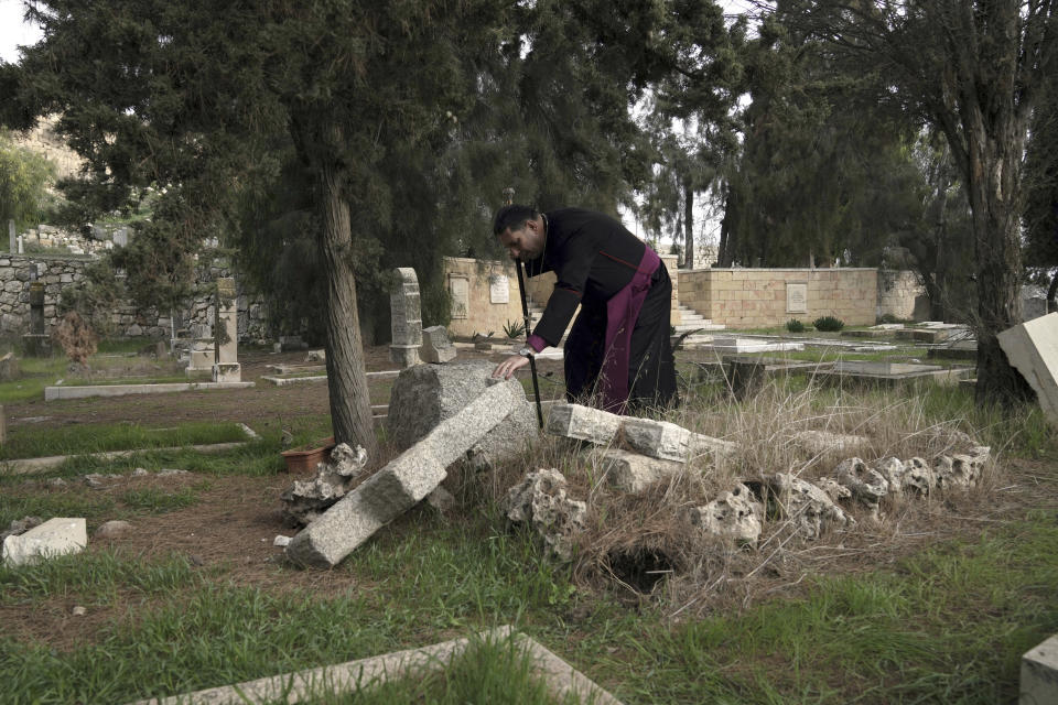 File - Hosam Naoum, a Palestinian Anglican bishop, touches a damaged grave where vandals desecrated more than 30 graves at a historic Protestant Cemetery on Jerusalem's Mount Zion in Jerusalem, Wednesday, Jan. 4, 2023. Israel's foreign ministry called the attack an "immoral act" and "an affront to religion." Police officers were sent to investigate the profanation. (AP Photo/ Mahmoud Illean, File)