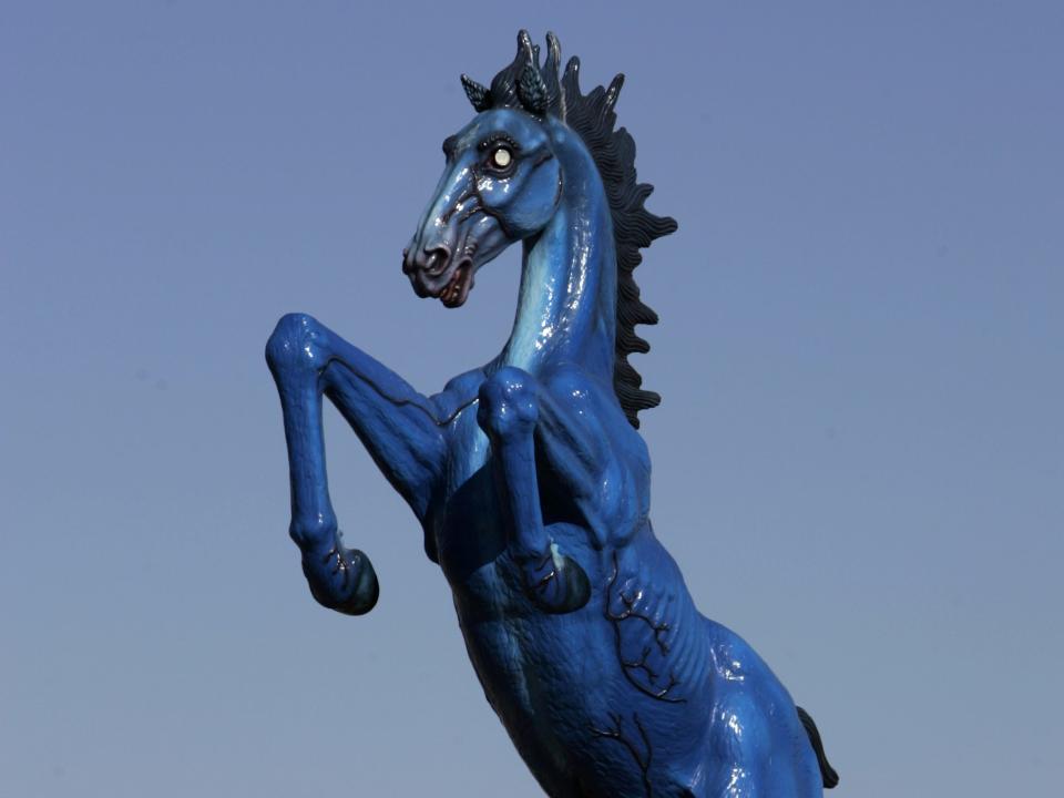 A large sculpture of a blue horse rearing up in front of a clear blue sky.